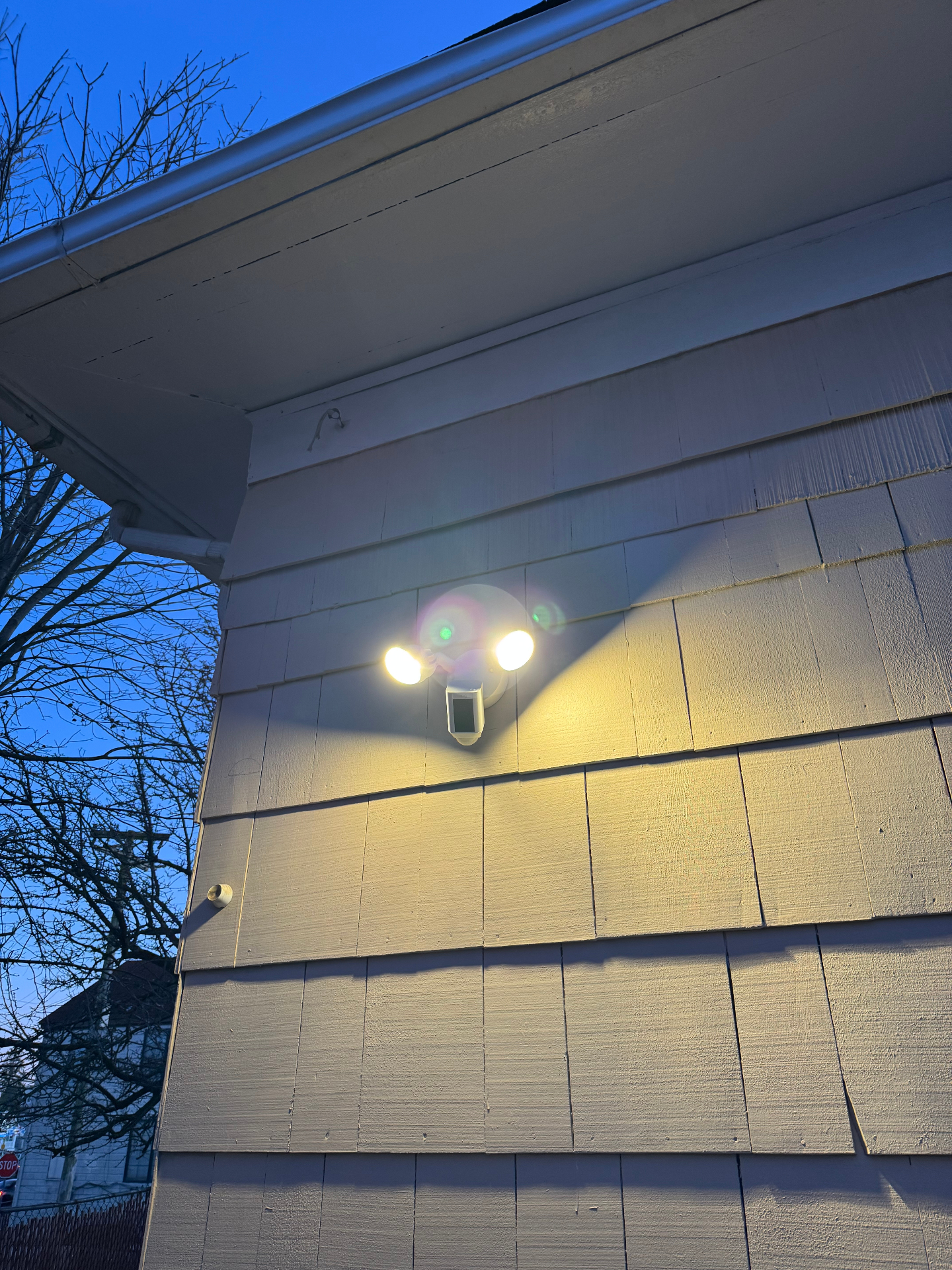 Residential floodlight security camera active at dusk on home siding