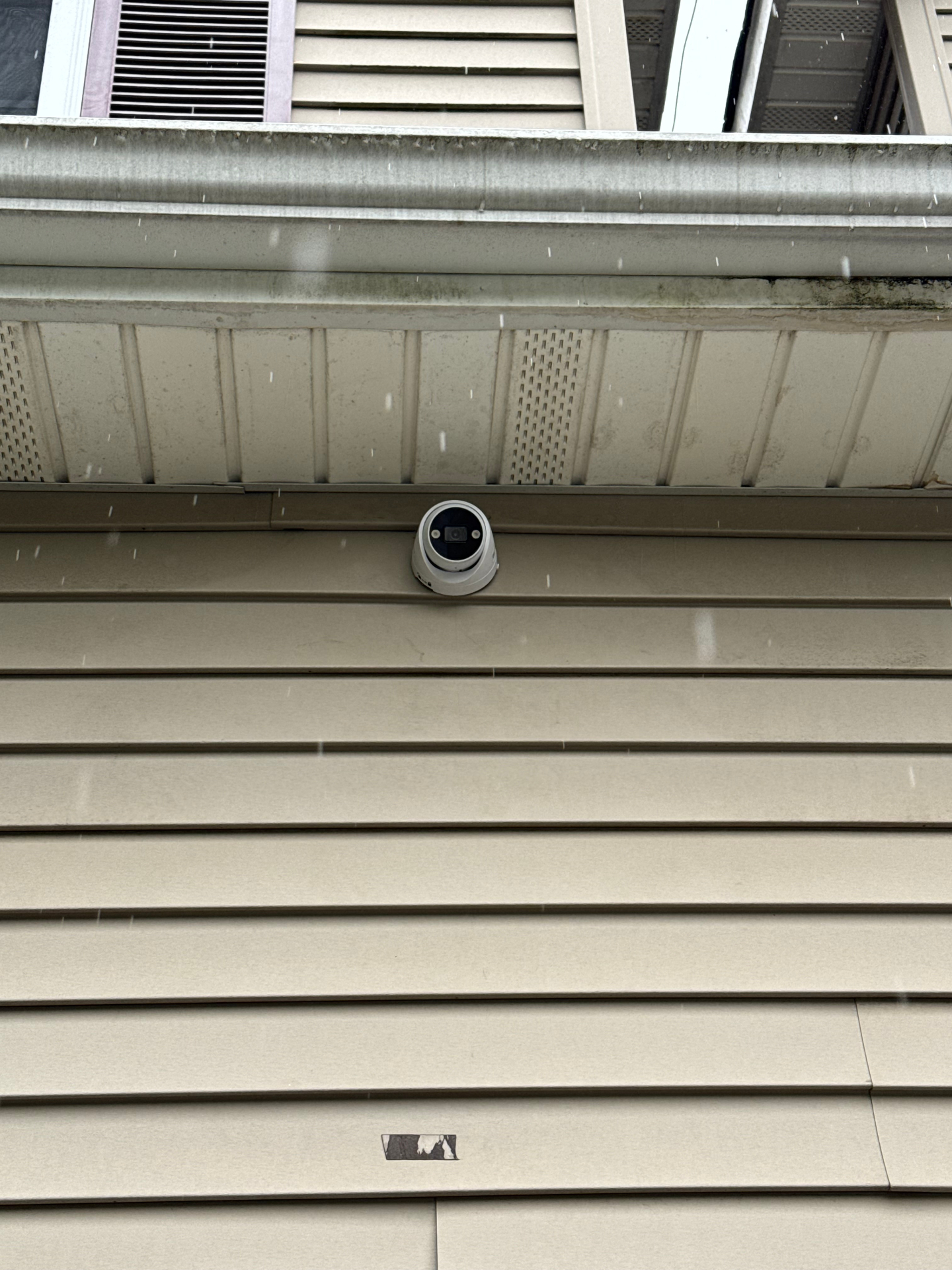 Residential turret dome security camera installed under home eaves on tan vinyl siding